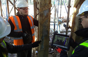 Men in high-visibility jackets and safety helmets looking at a laptop during refurbishment of old timber-framed building