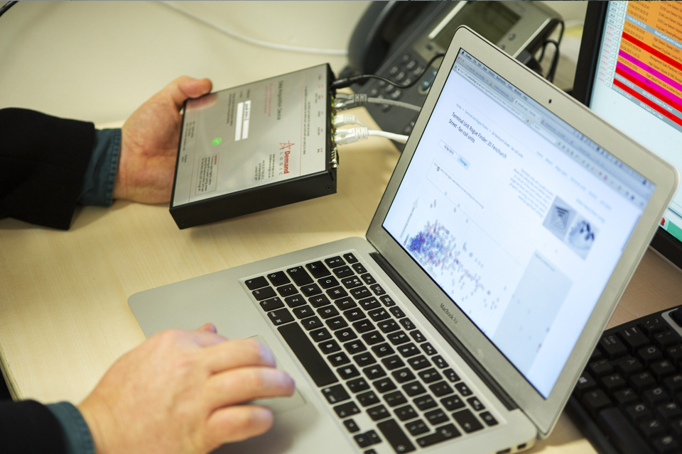 Male hands operating hardware and laptop with Demand Logic visualisation software on screen.