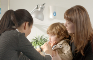 A child sitting on a woman's lap getting a nasal spray