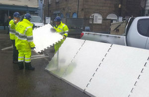 Three men in Environment Agency uniform building a short wall of barriers across a road in Fowey