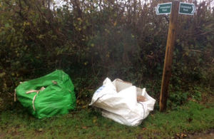 Two very large builders' waste bags left by roadside next to fingerpost