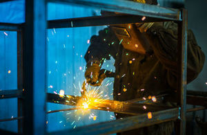Worker in overalls and protective mask welds metal