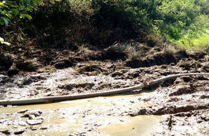 A brown, rusty pipe crossing left to right in a picture of a muddy field