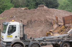 Picture of a branded skip carrier parked in front of a large pile of brown waste