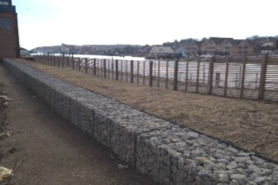 Rock-filled wire mesh boxes used to construct flood defences at edge of sea bay