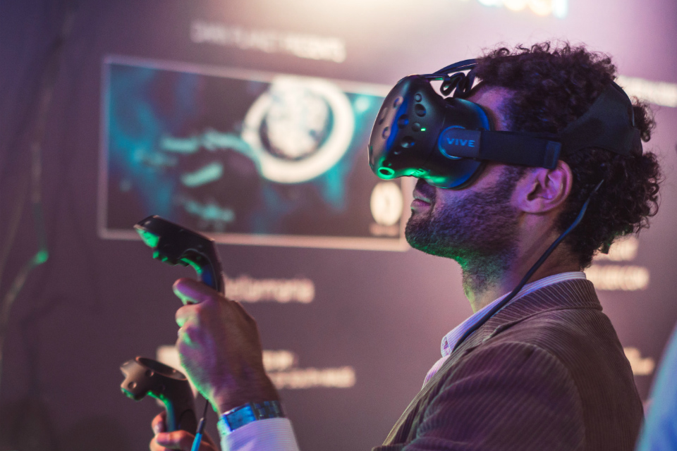 A man in a virtual reality headset holding 2 wireless controllers.