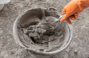 Hand with trowel and bucket with mortar at construction site