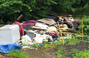 Piles of rubbish stacked waist-high in front of green bushes