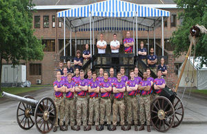 18 military personnel posing beside a cannon.