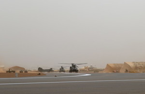 Three Chinook helicopters on a runway in Mali. The background is hazy and there are tents in the background that are desert-camouflaged