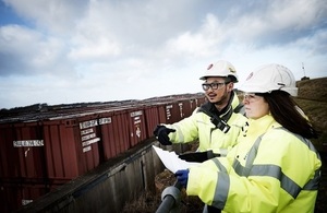 Two members of the LLWR workforce in hard hats, safety gloves and jackets look out over Vault 9 on the Repository Site