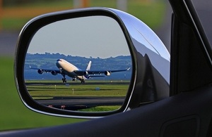 An aeroplane taking off reflected in the side mirror of a car