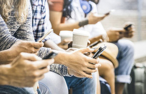 A row of people holding coffee cups and using their smartphones.