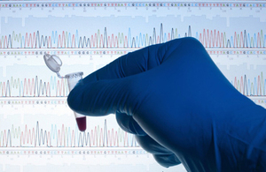 A hand wearing a surgical glove holding a test tube in front of some genetic data