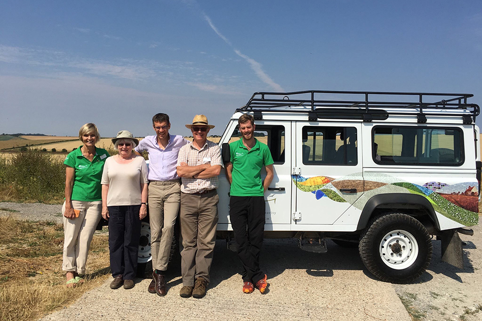 Panel team standing by a car in front of open countryside