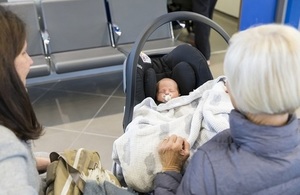 A baby in a car seat in a GP waiting area being watched by its mother and grandmother.
