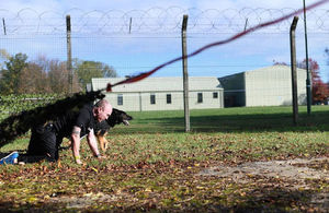 Ministry of Defence policeman and his dog scrambling through the cargo net.