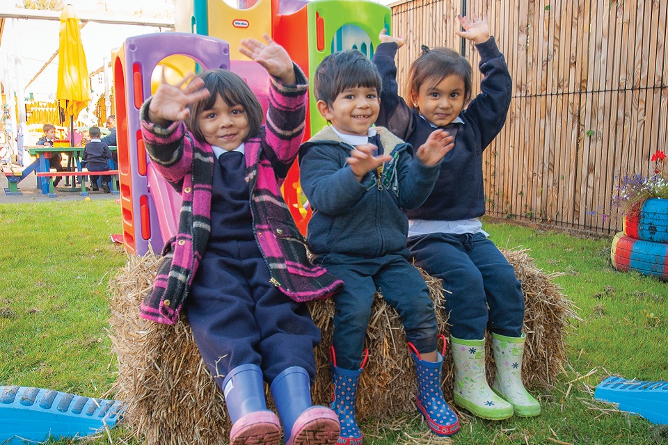 Three young children outside sitting on hay bale