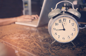 Old alarm clock with person typing on laptop in background