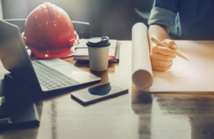 Desk with laptop, safety hat, mobile phone and office plans