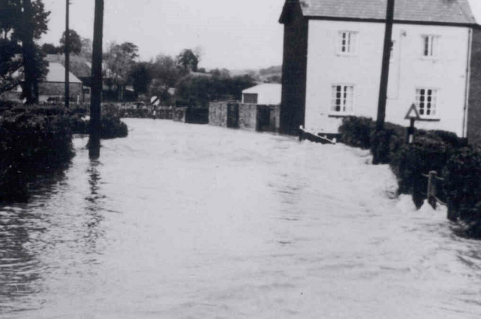 Black and white photograph of flood water flowing through Colyton in 1968