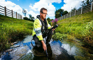 Environment Agency officer in Hi-via jacket using monitoring equipment in a stream