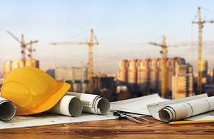 Construction backdrop with hard hat and rolls of blue prints on table.