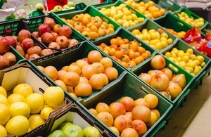 A variety of fruit, including oranges and lemons, in green boxes on supermarket shelves