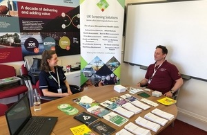 Occupational health technician, surrounded by informative leaflets, speaks to a member of LLWR workforce