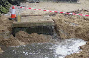 Picture of the manhole on beach leaking sewage into a shallow hollow dug around it in the sand