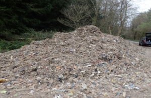 A heap of shredded waste with a road, trees and a car in the background.