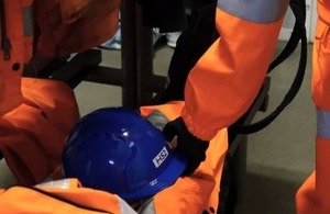 Arm and hand in protective clothing reaching down to grab a hard hat with HS2 logo on it