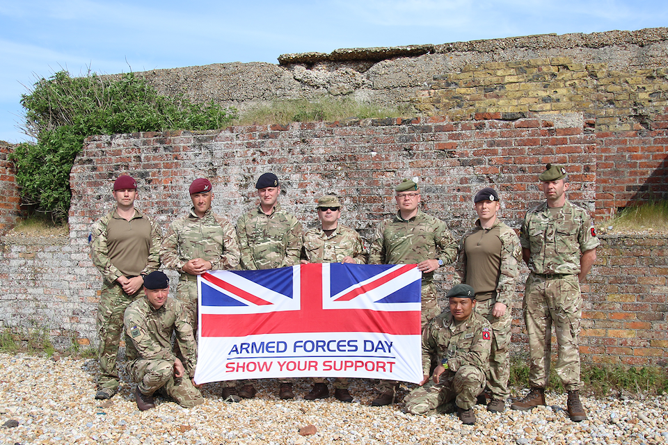 British Army soldiers and officers take a photo with the Armed Forces Day flag. 