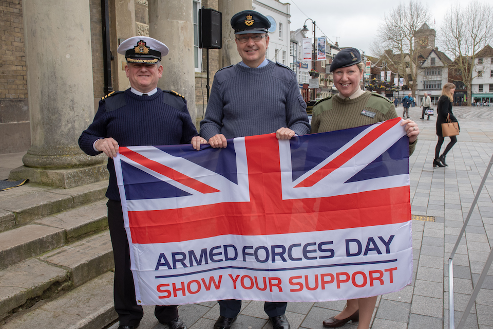 Personnel from the Navy, RAF and Army take a photo with the Armed Forces Day flag.