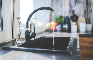 A black tap with water running from it, with a bottle with a flower in it and kitchen utensils in the background