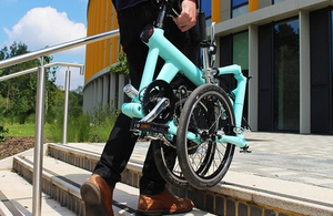 Man carrying folded electric bicycle up stairs towards the entrance of an office building