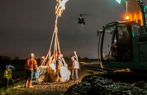 Image of chinook helicopted dropping sand bags, and a tractor with people standing by.