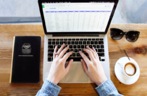 Hands typing on laptop with computer screen showing spreadsheet