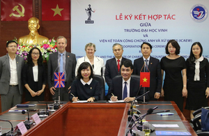 Minister Heather Wheeler with Ambassador Gareth Ward and others at Vinh University as 2 people sign documents