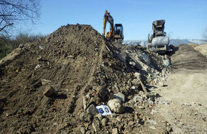 Picture shows large pile of earth to the left with a digger on top, with processing machinery to the right