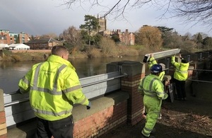 Four members of staff in high-vis jackets constructing temporary barriers near a river