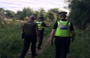 Two police officers walking alongside a river bank