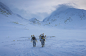 Royal Marines dressed in all white march against a backdrop of snow-covered hills and ice blue skies