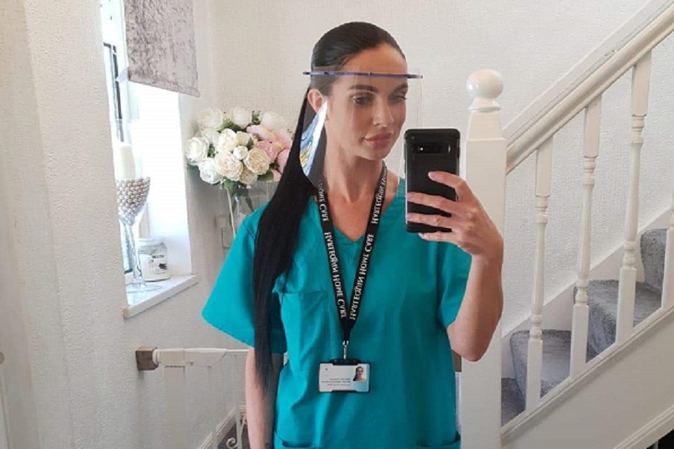 A selfie taken in a mirror of a health care worker in full uniform wearing one of the 3D printed visors