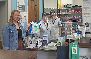 Portrait image of Amy Caddy standing in a pharmacy handing over a bag of prescriptions