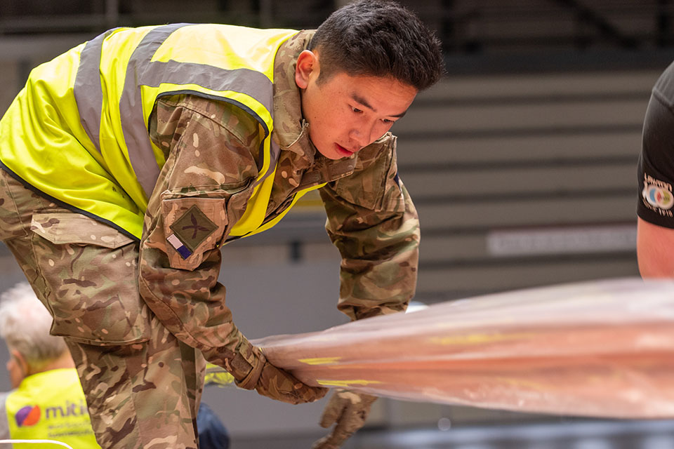 A British Army soldier lifting a length of copper pipe