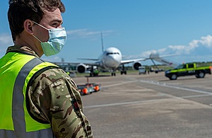 An soldier wearing hi-visibility jacket, PPE and face mask standing on a runway.