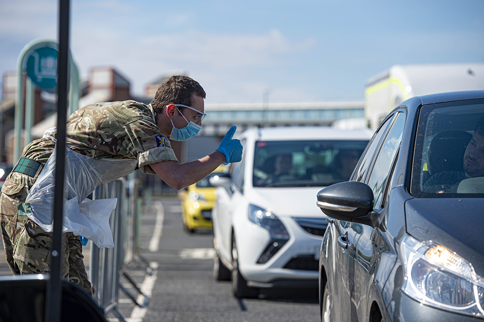 A soldier looks looks into the driver window of a car, giving a thumbs up. 