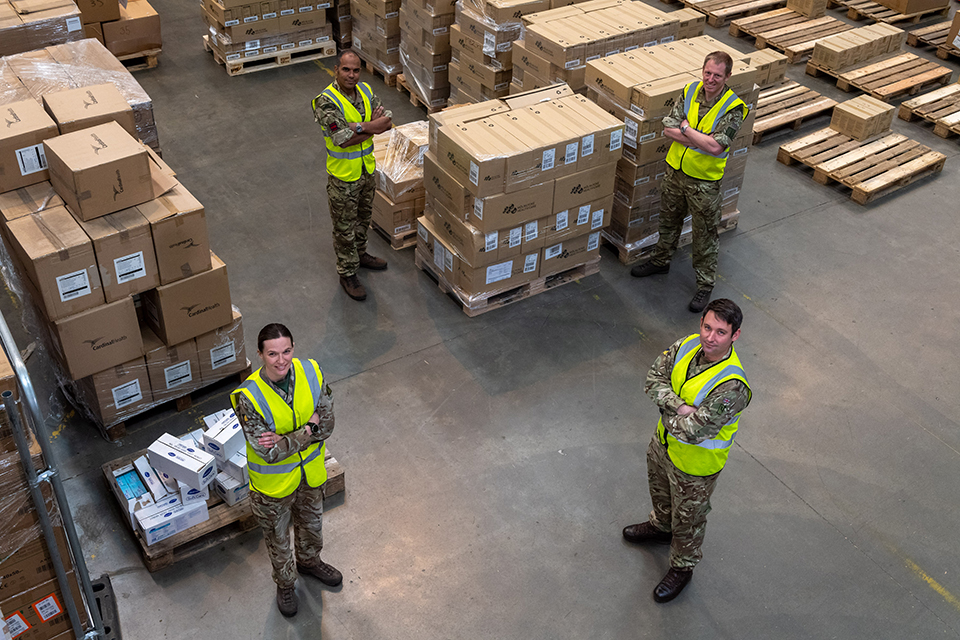 Soldiers stand surrounded by boxes of PPE.