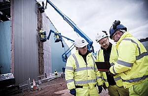Image of a construction site with 3 employees standing in the foreground